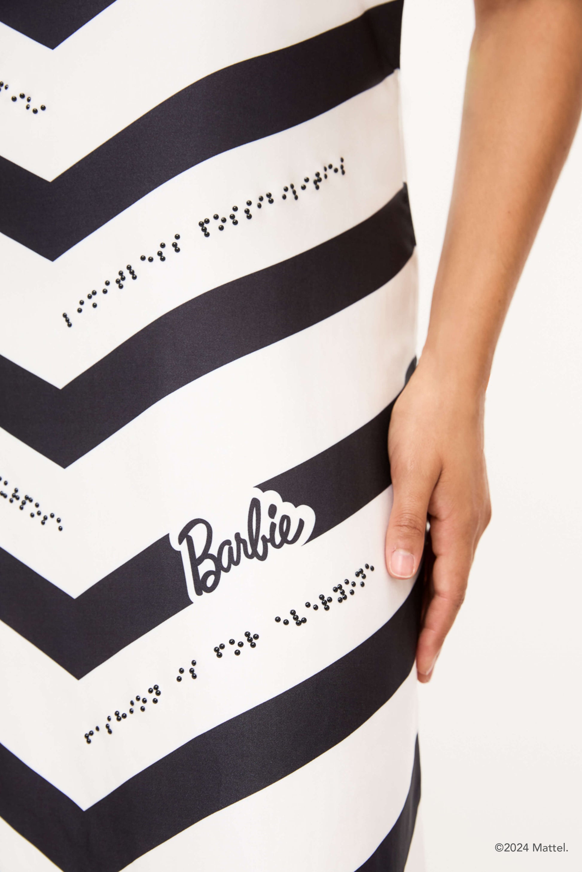 A close-up of the black and white chevron dress focusing on the detailed braille beadwork and "Barbie" logo.