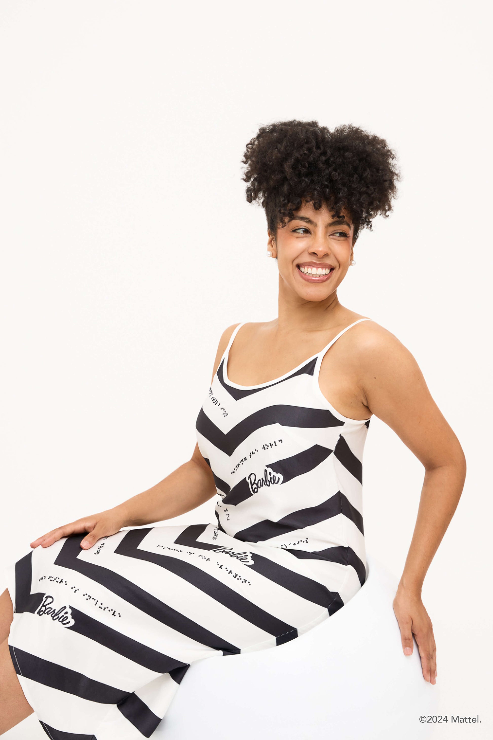 Model sits and smiles while wearing a black and white chevron dress with black braille