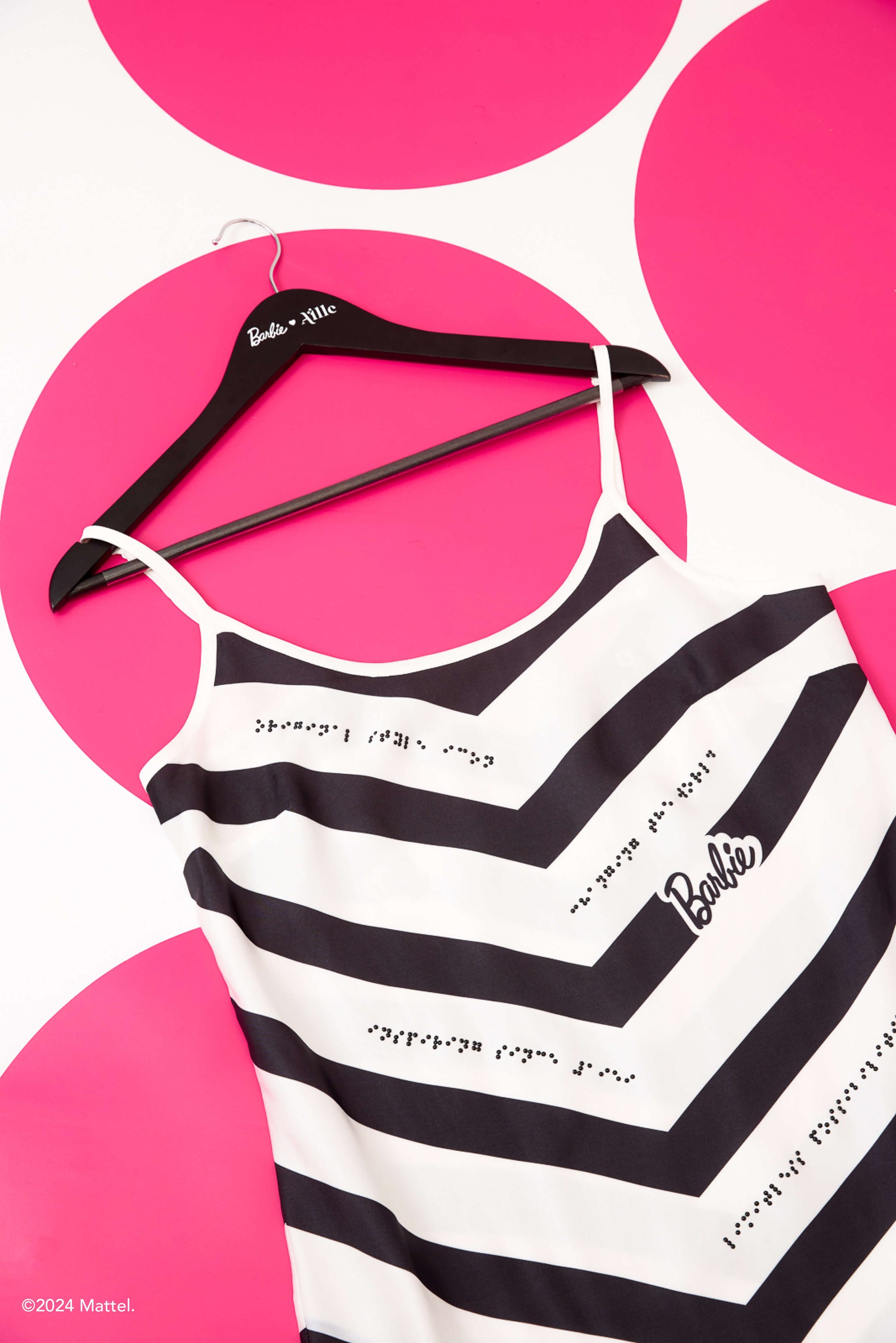 Black and white chevron-patterned dress with black braille beadwork. Dress is on a black hanger against a pink polka dot background.