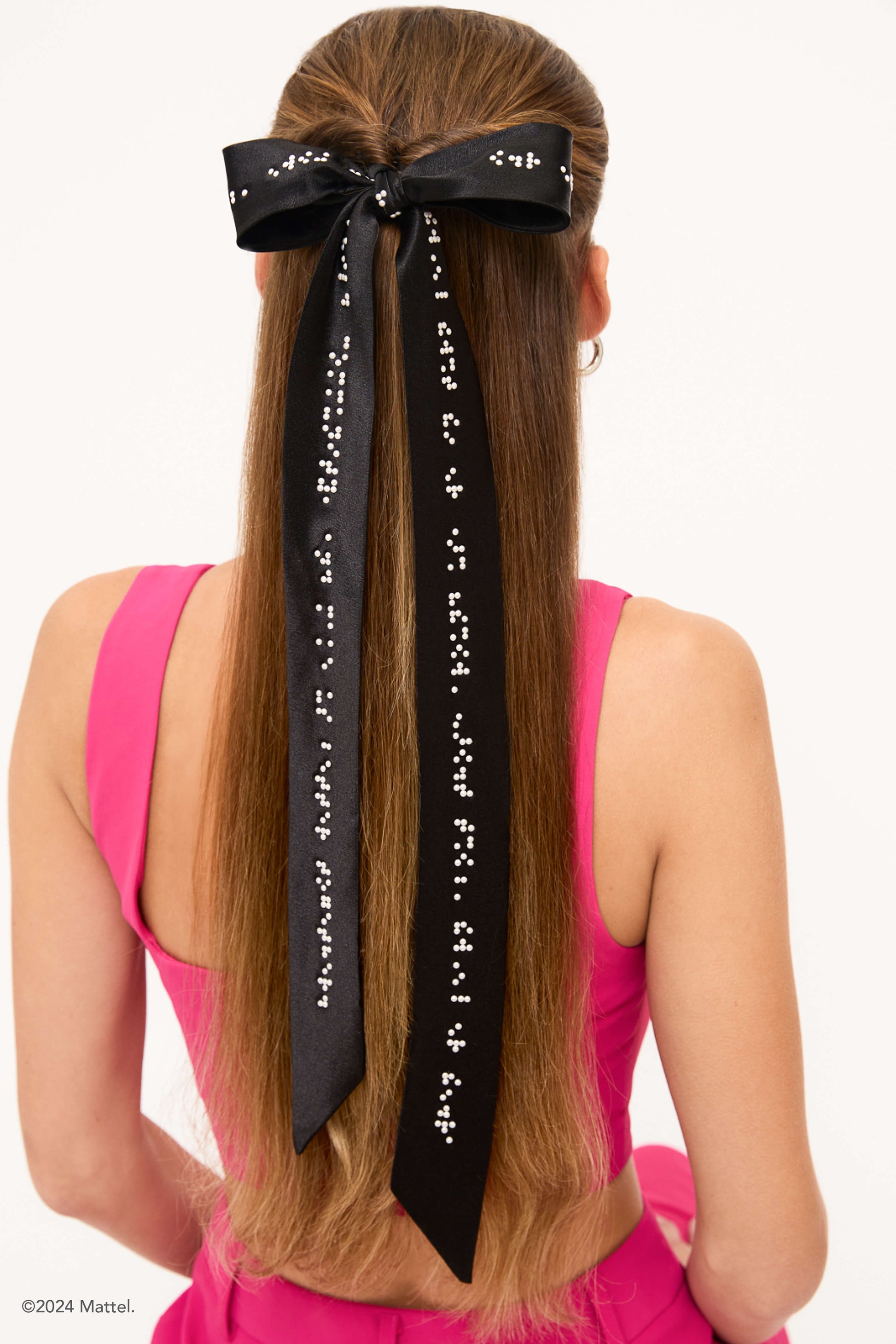Back view of a woman wearing a long black bow with white braille in hair.