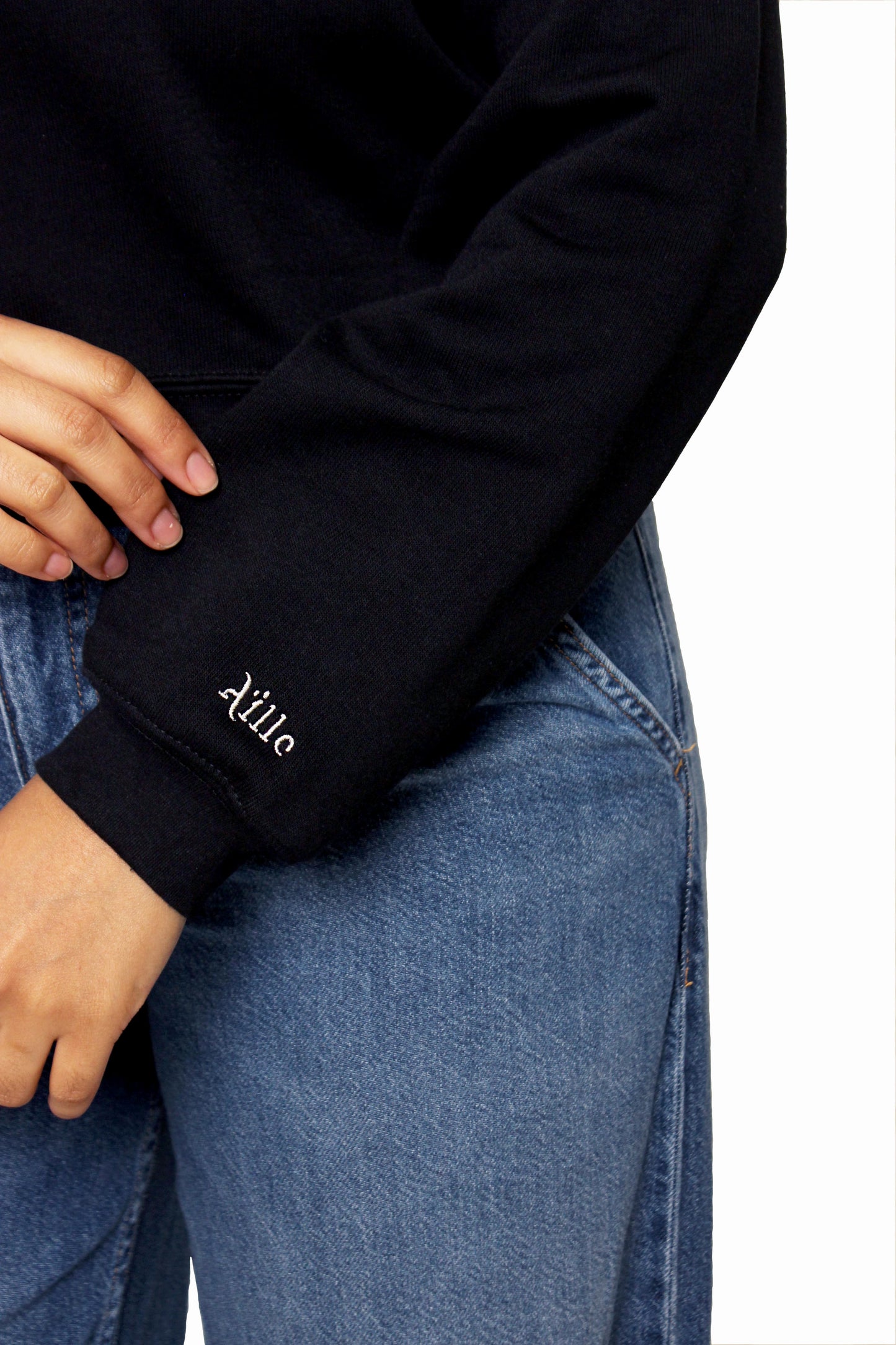 Close up of Aille Design logo embroidered in white on the cuff of the left sweater sleeve.