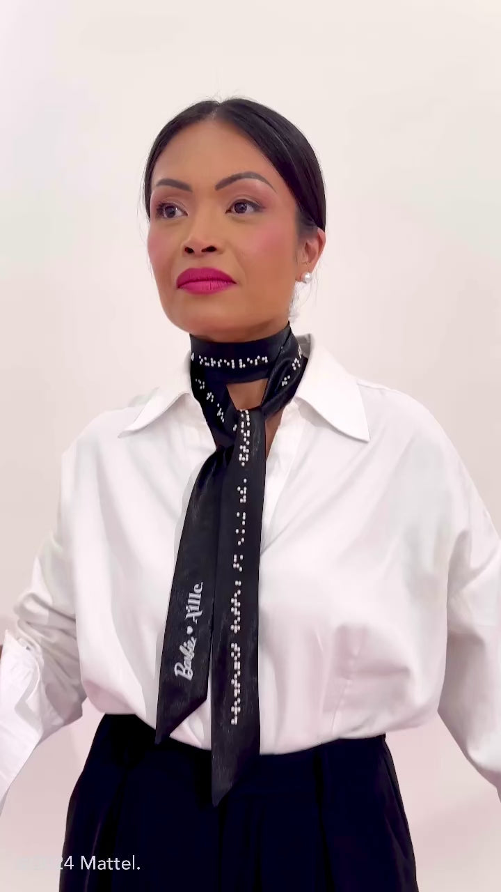 Blind model moves around on pink polka dot photoshoot set showcasing the black scarf with white braille and the many ways it can be tied.