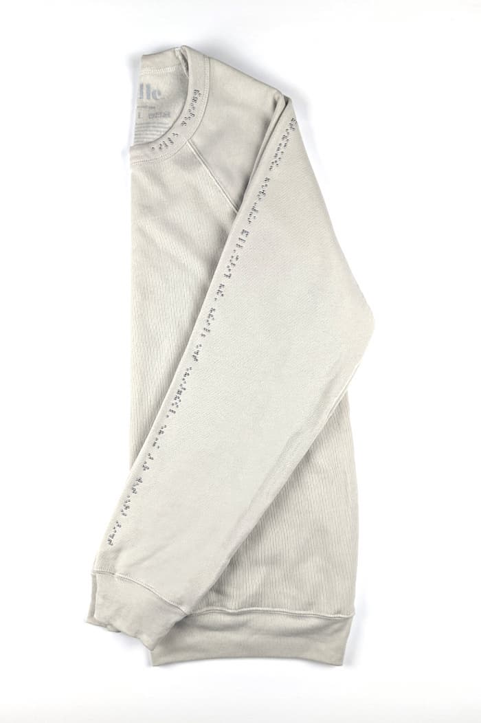 Beige sweater with chrome braille along one sleeve and half of neck