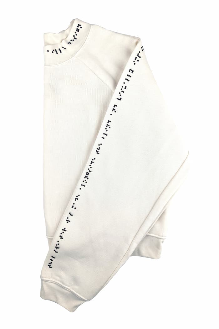 Cream sweater with black braille along one sleeve and half of neck