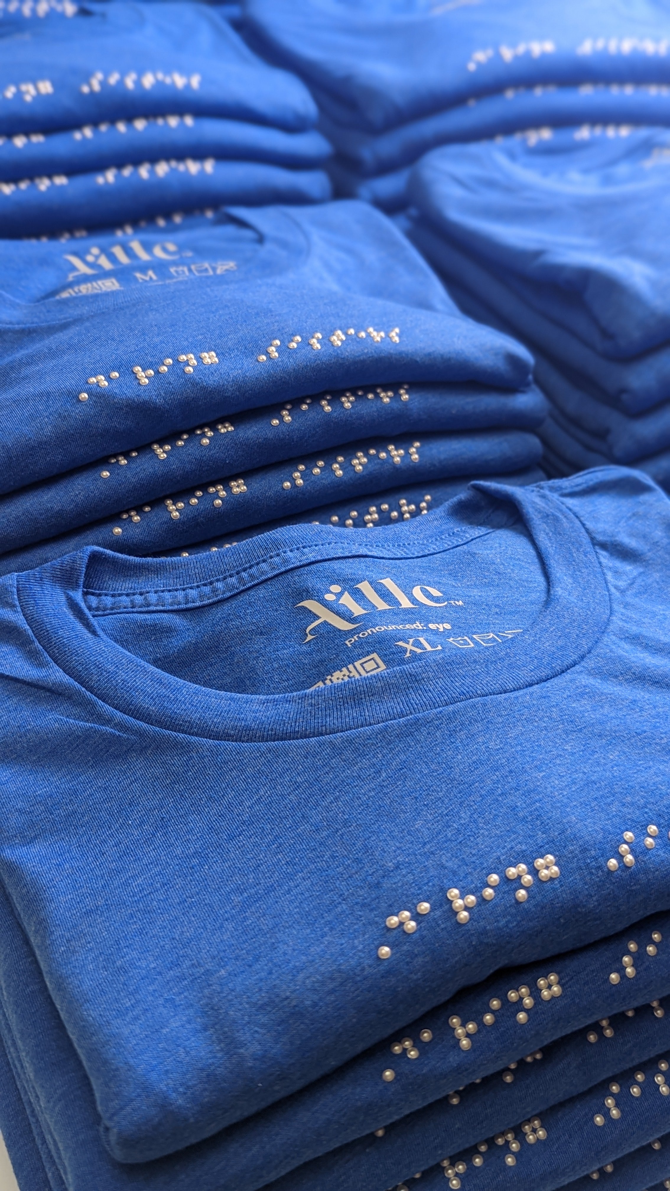 Stack of royal blue t-shirts with white braille beadwork