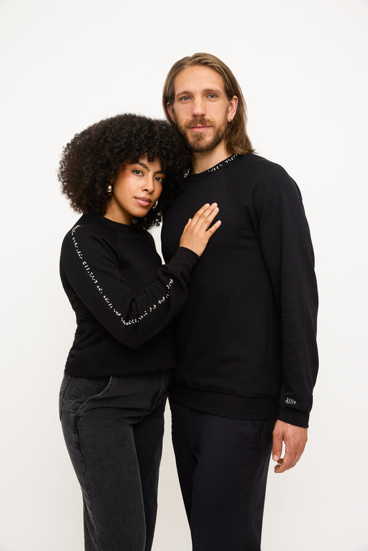 A women wearing a black crewneck sweater with white braille beads rests her head on a man wearing a black crewneck sweater with white braille beads.