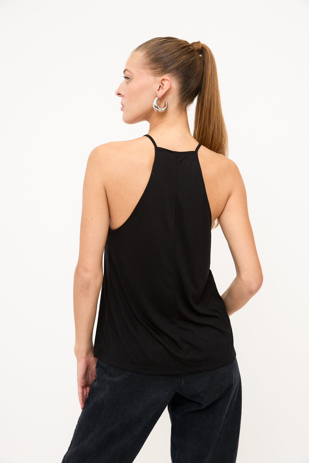 Back view of blind model wearing a black racerback tank top, silver hoop earrings, and slicked back ponytail.