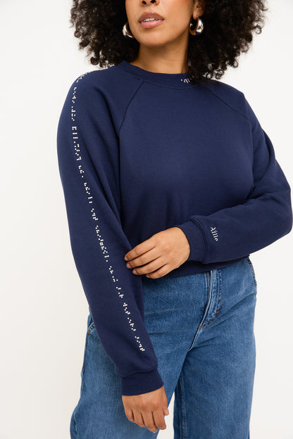 A model wears a navy blue cropped sweater with white braille beads paired with a high waisted blue jean