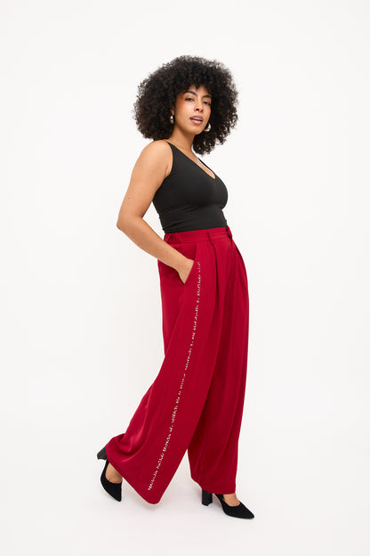 Full body side view of the red wide-leg pants, highlighting the white braille beadwork tuxedo stripe.