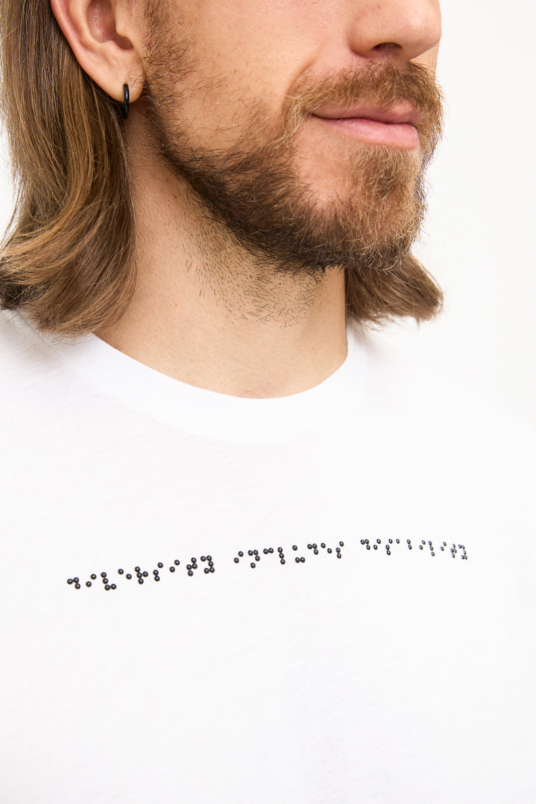 Braille Detail on White T-Shirt: Close-up of black braille beadwork on shirt reads "diversity includes disability".