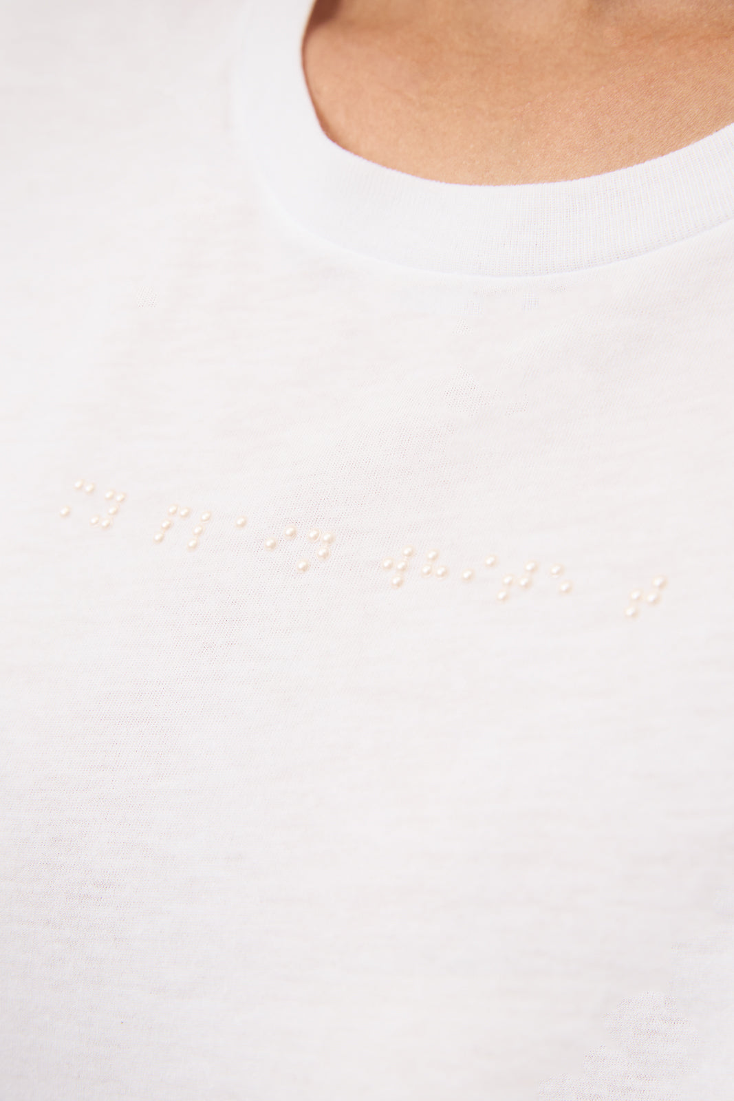 Close up of white T-shirt with white braille beadwork that reads "my plain white t".