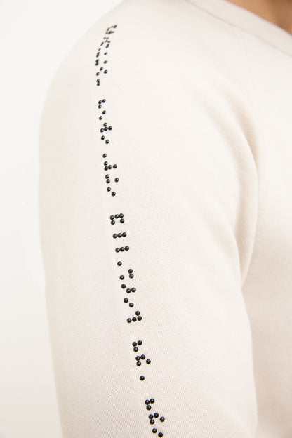 Close up of black braille beadwork detailing on the right sweater sleeve where it meets the shoulder.