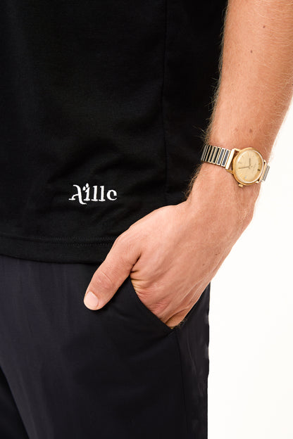 Logo Detail on Black T-Shirt: Close-up of the bottom corner of a black t-shirt showing the "Aille" logo in white embroidery