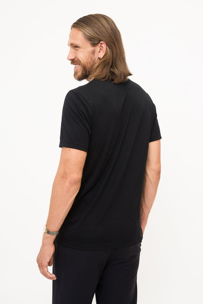 Back View of Black T-Shirt: Young man with shoulder-length hair looking over his shoulder, showing the back of a black t-shirt.