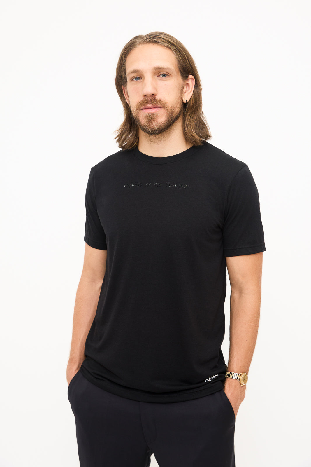 Front View of Black T-Shirt: Young man standing, hands in pockets, wearing a black t-shirt with black braille beadwork on the chest.