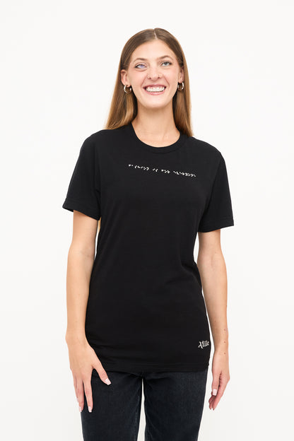 Front View of Woman's Black T-Shirt: Young blind woman smiling, wearing a black t-shirt with white braille beadwork below the neckline.