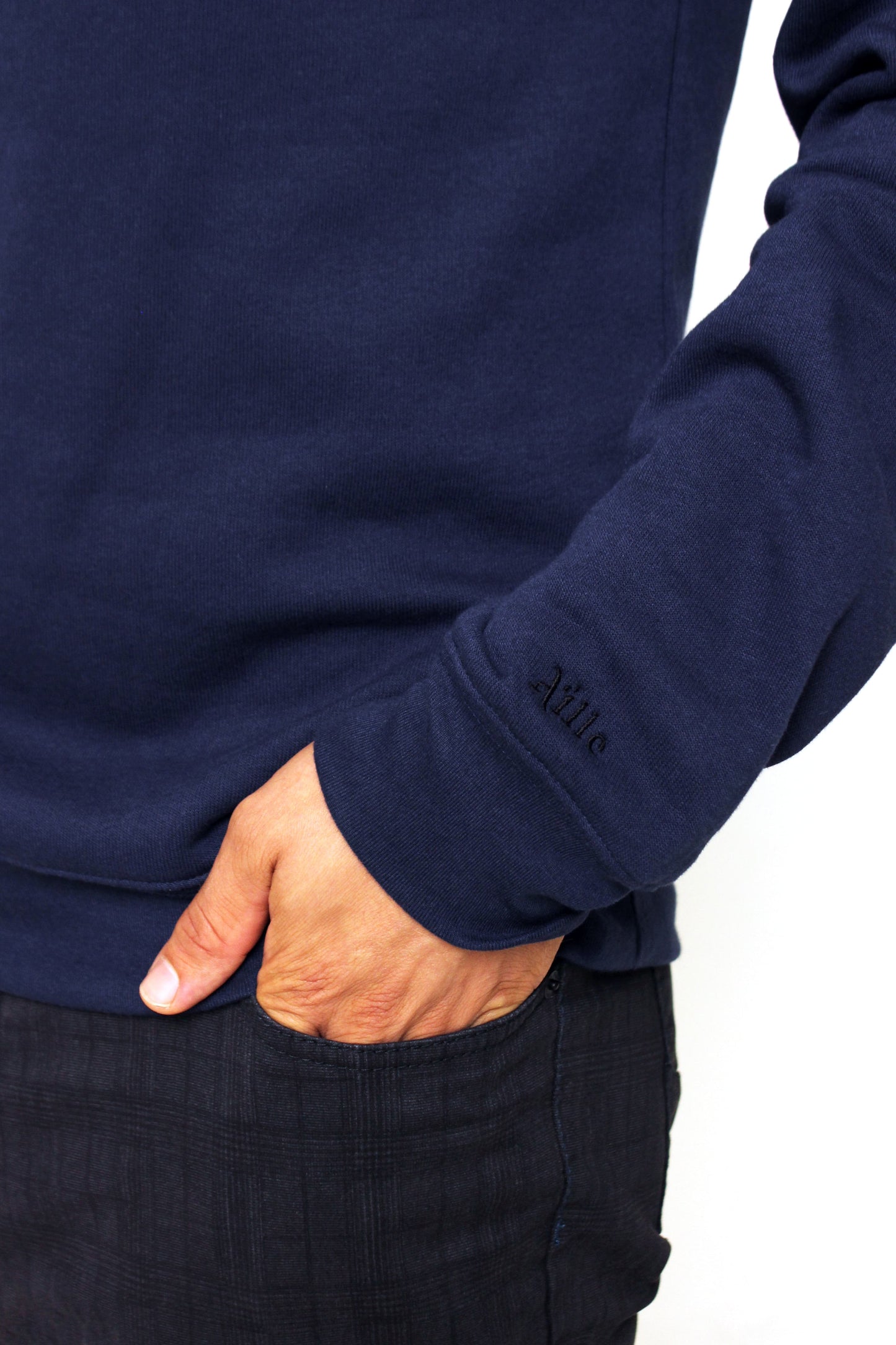 Close up of Aille Design logo embroidered in black on the cuff of the left sweater sleeve.