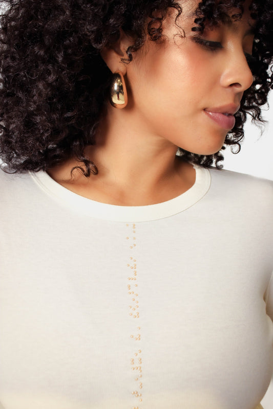 Close up of model wearing gold braille beadwork on cream shirt
