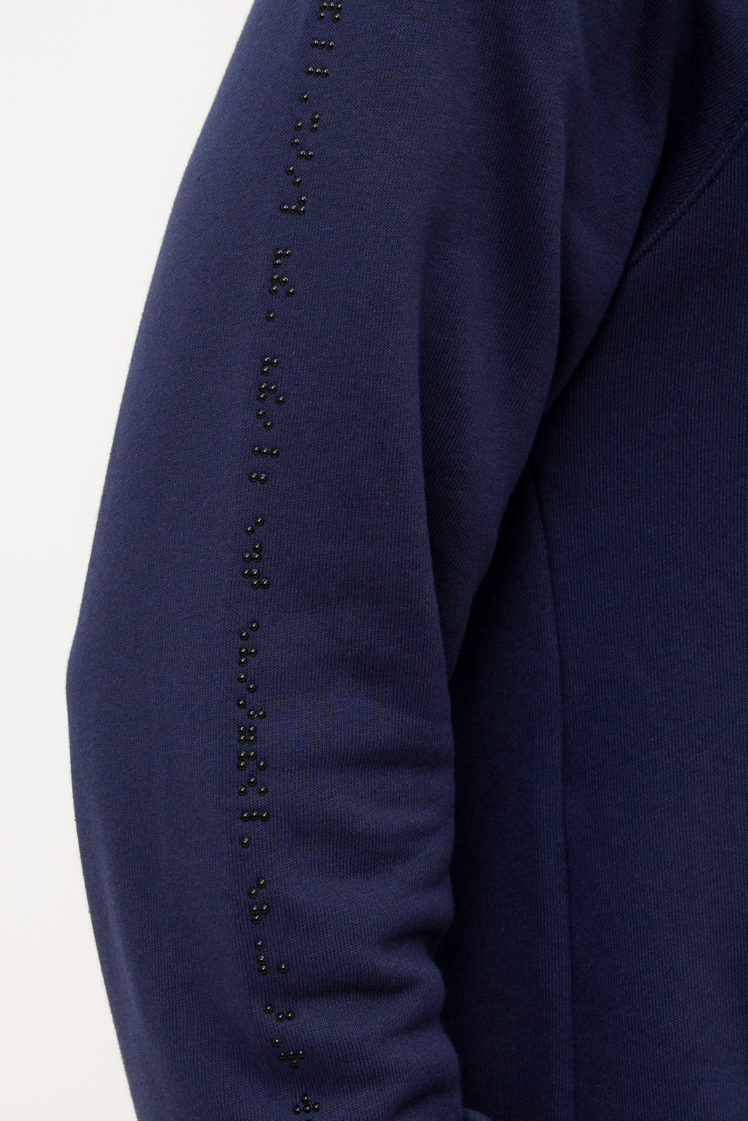 Close up of black braille beadwork on the right sleeve of a navy blue sweater. The braille starts at the cuff and goes to the shoulder.