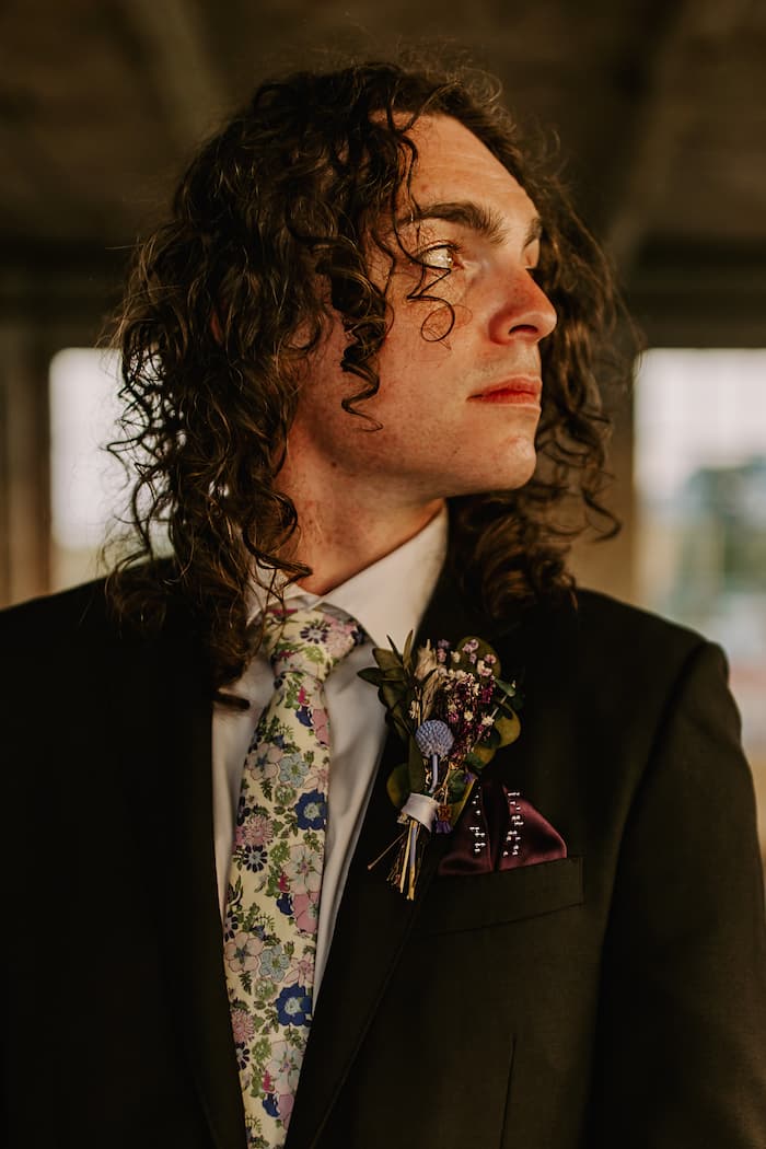 Groom wears black suit with dark purple pocket square for his wedding