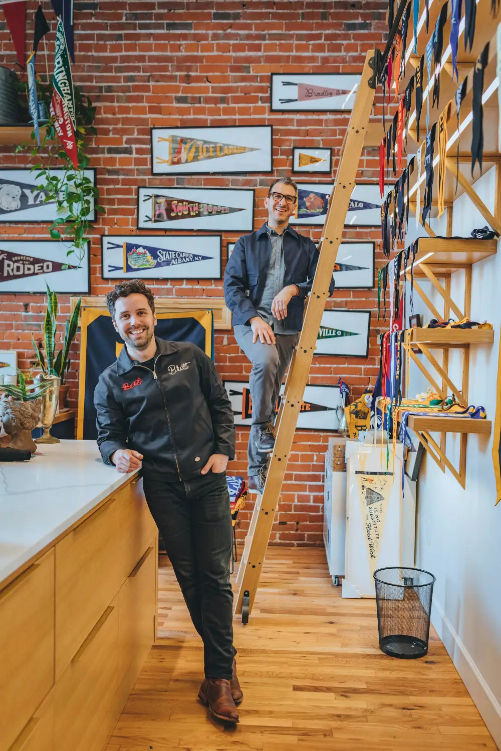 Oxford Pennant team members standing inside brick studio with framed felt pennants.