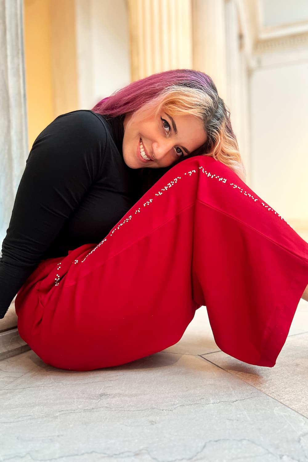 Model sitting with bent knees in the red pants