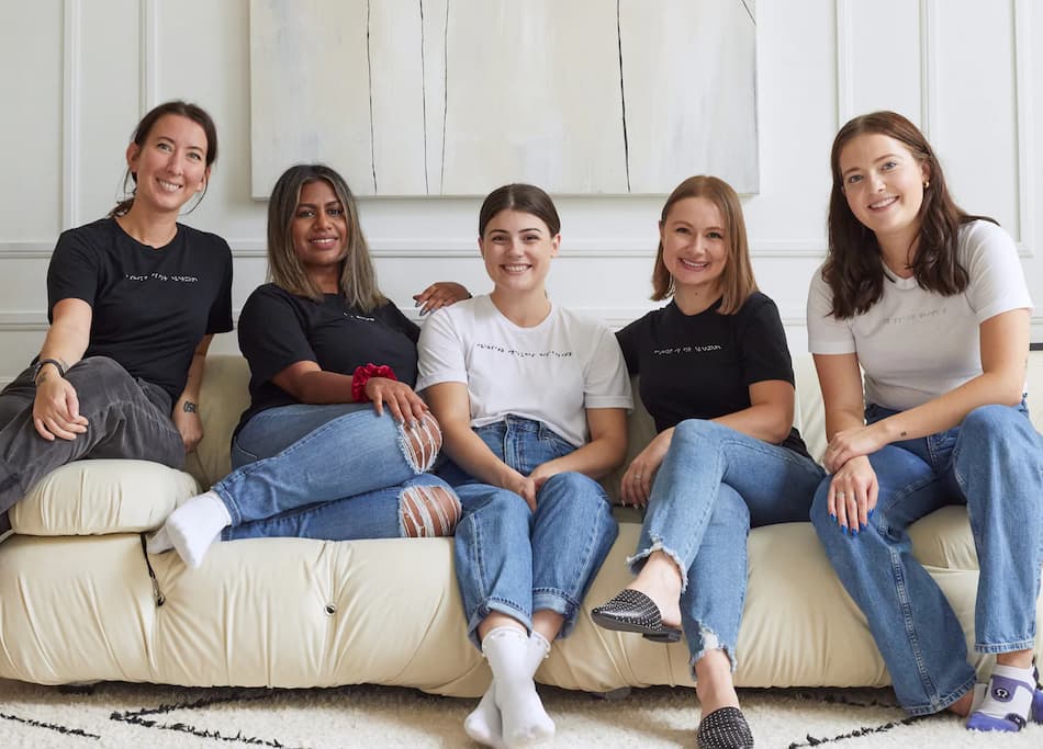 Blind and sighted women sitting together on couch wearing braille t-shirts