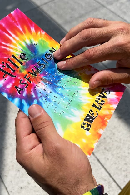 Close up of tie dye card with braille that reads Aille x ASFVISION