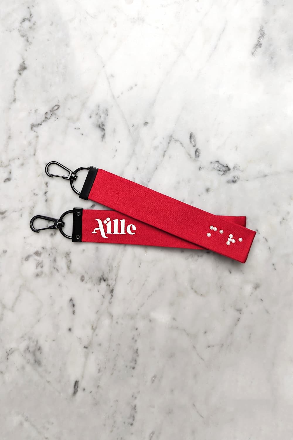 Red keychain with white braille on one side and a white screen printed Aille Design logo on the other side.