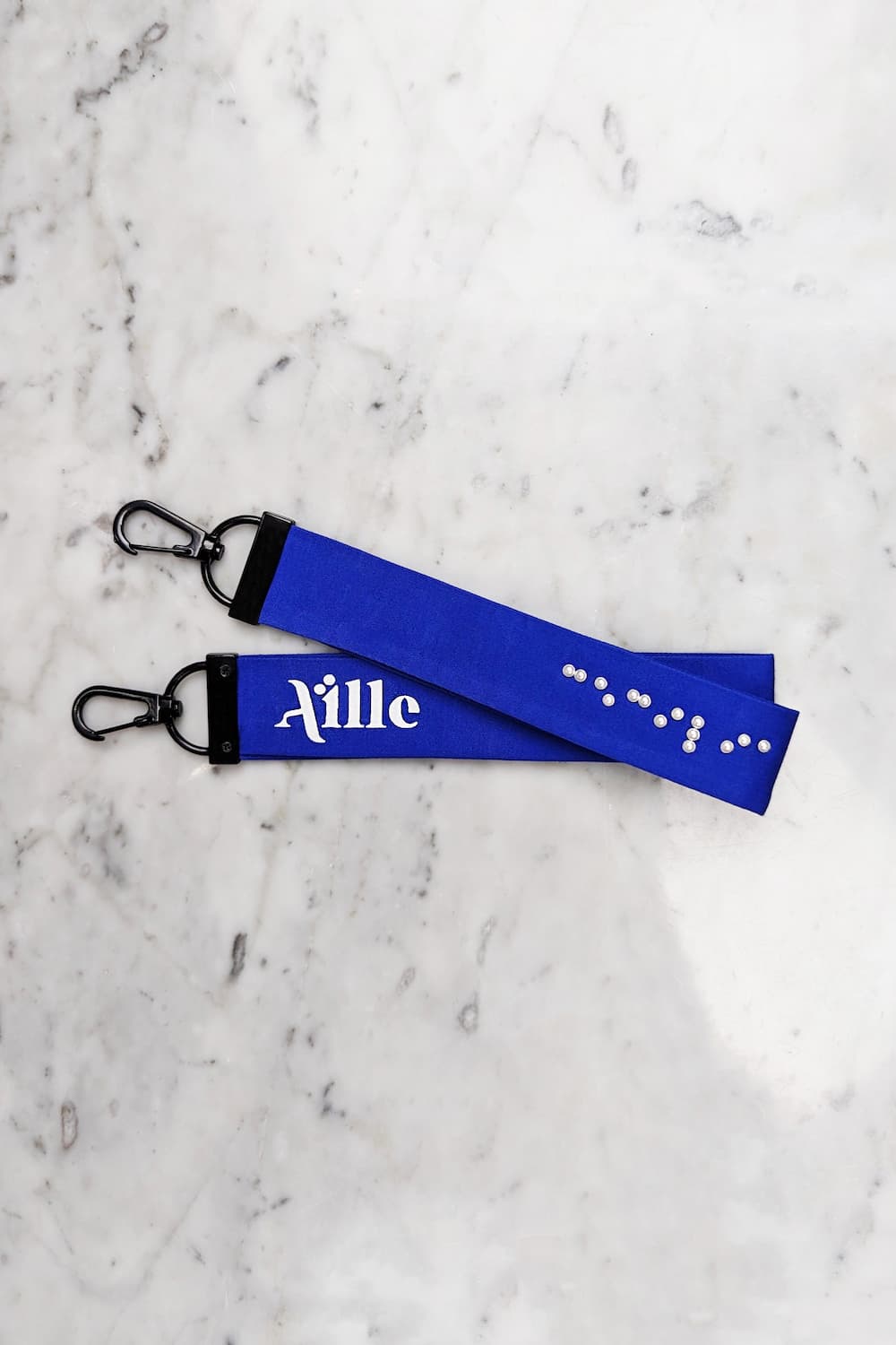 Royal blue keychain with white braille on one side and a white screen printed Aille Design logo on the other side.