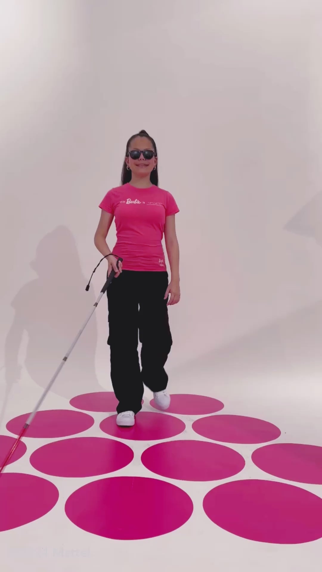 Blind model Lana moves around on the pink polka dot photoshoot set and reads the braille on the Barbie t-shirt.