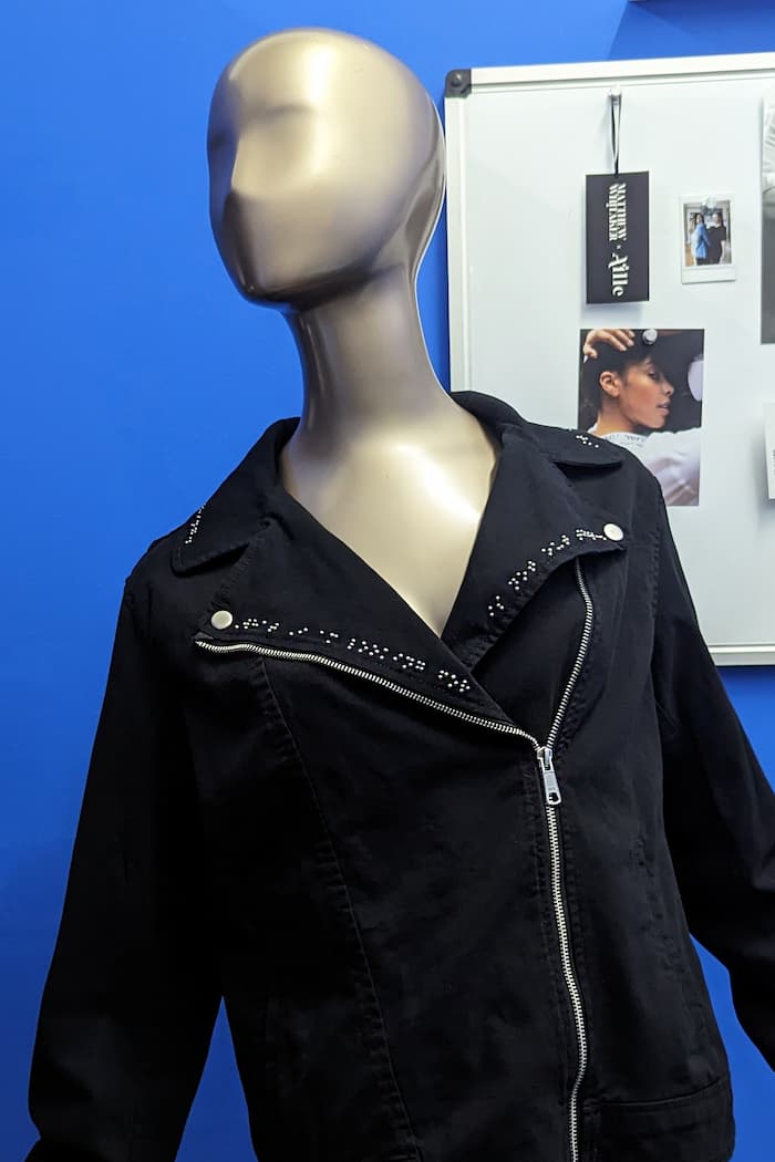 Braille clothing that is a black denim motto jacket with exposed zippers and dark grey braille