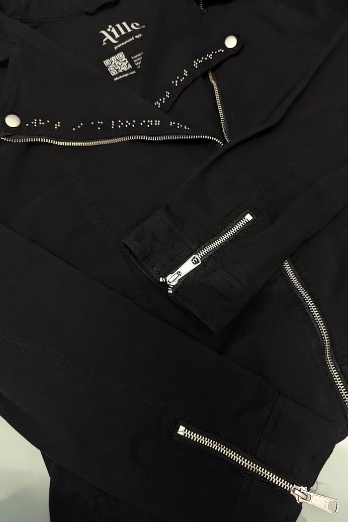 Exposed zippers on sleeve cuffs of denim braille jacket