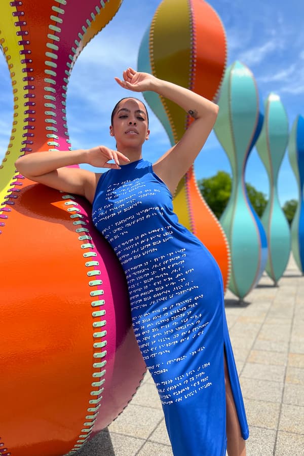 Latina woman wearing blue braille dress next to colorful sculptures
