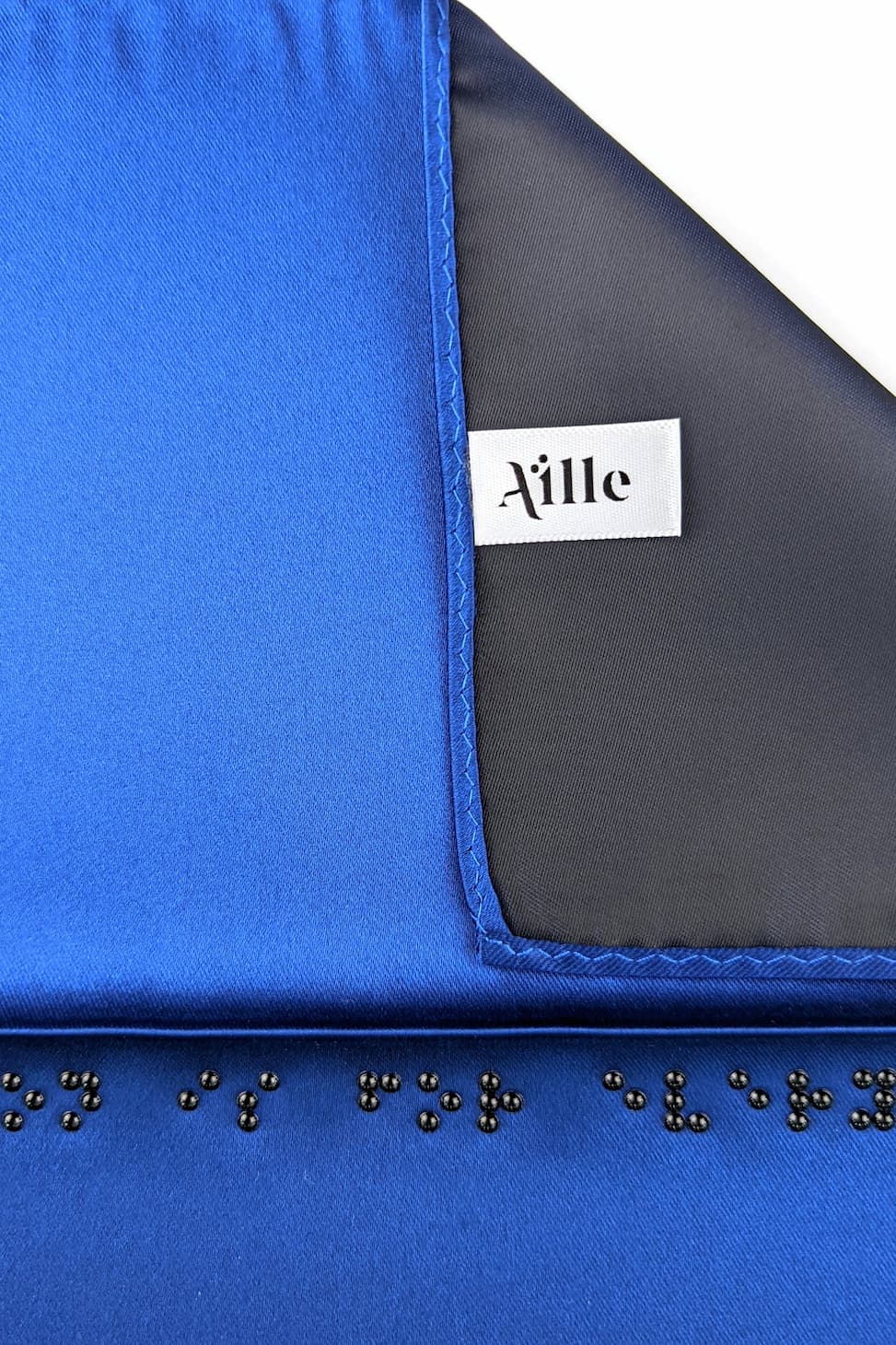 Detail photo of blue pocket square with black braille. White Aille Design tag on reverse side.