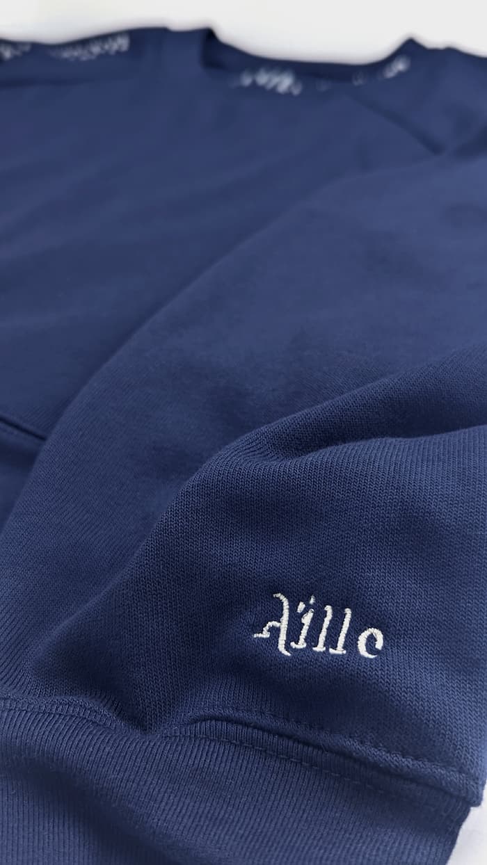 Silver embroidered logo on cuff of navy blue braille sweater