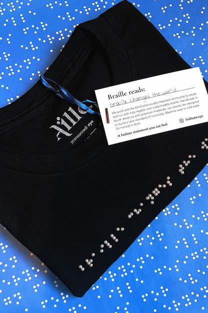 Folded black braille t-shirt on blue simulated braille tissue paper. Braille beadwork reads: braille changes the world