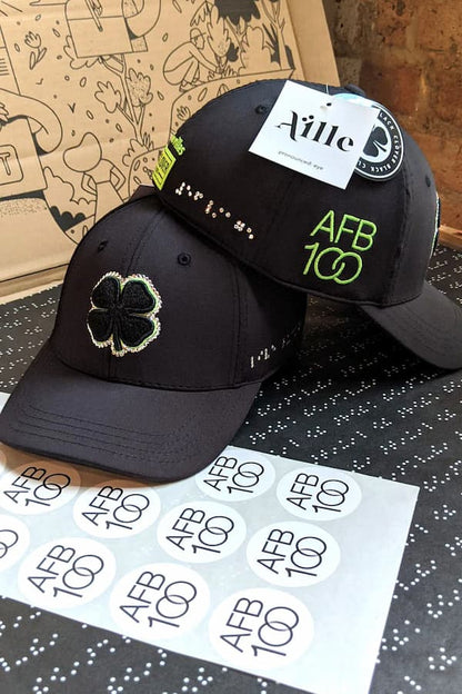 Black hat with silver braille next to AFB100 stickers