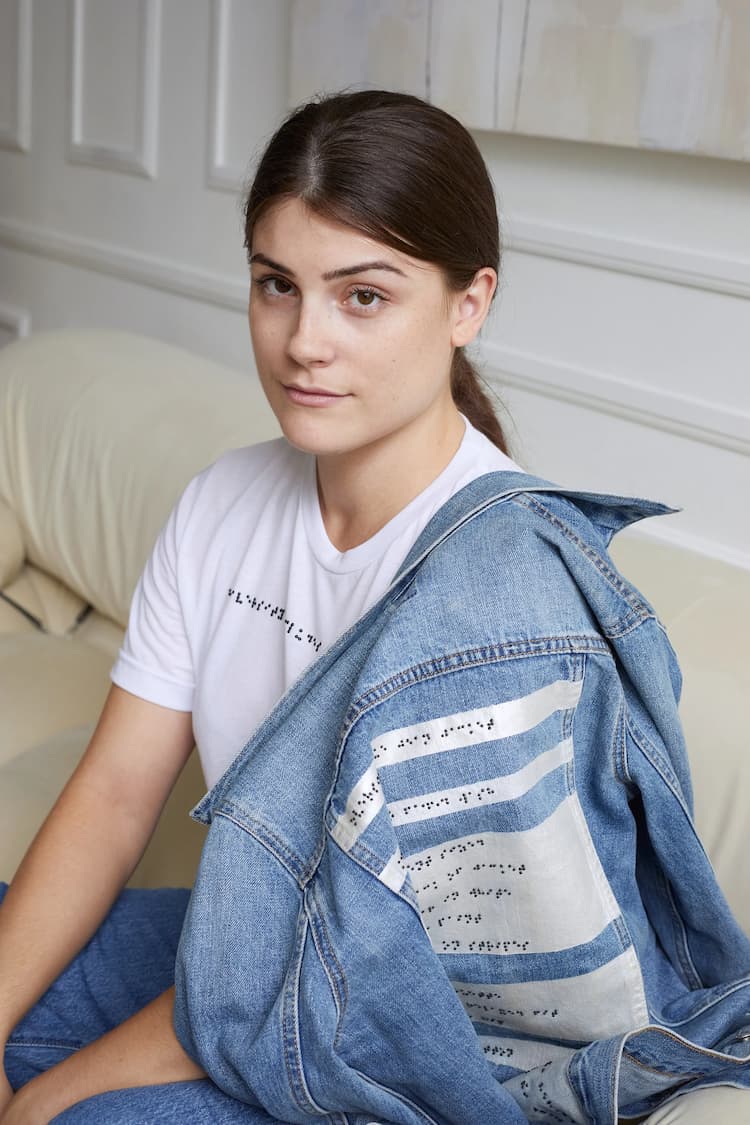 Visually impaired white woman wearing white braille t-shirt and braille denim jacket