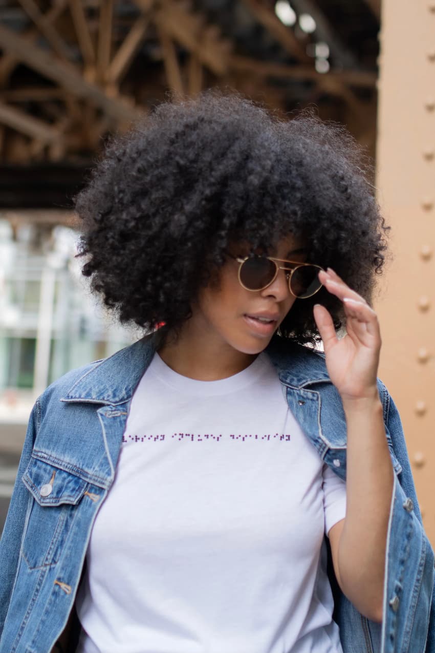 Black Latina woman wearing white braille t-shirt and sunglasses