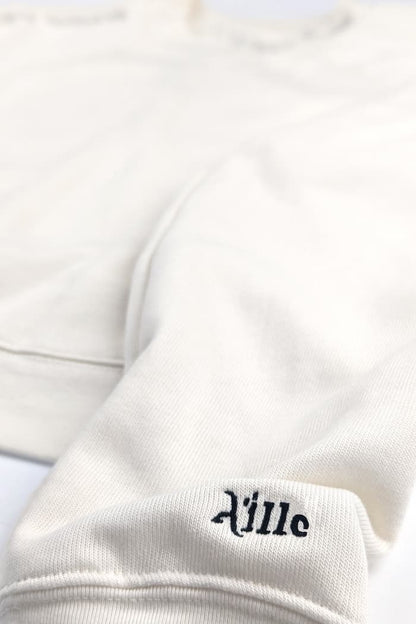 Black embroidered logo on cuff of cream braille sweater
