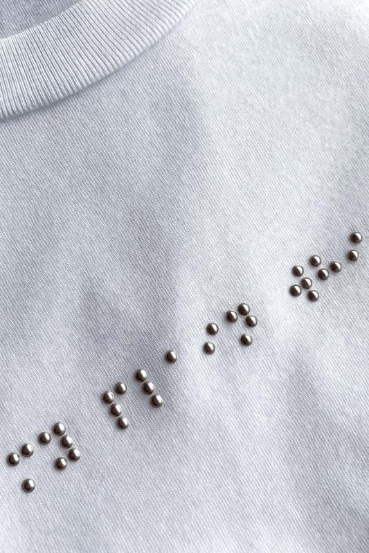 Close up of silver braille on white t-shirt that reads my plain white t.