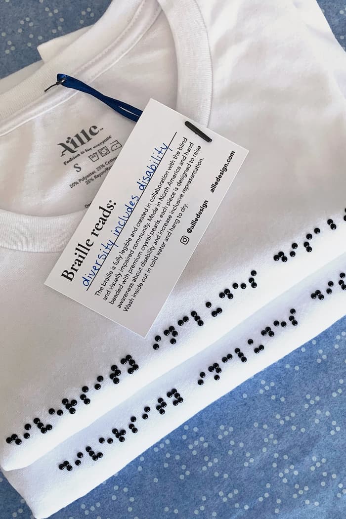 Two folded t-shirts on braille tissue paper. T-shirts are white with black braille beadwork.