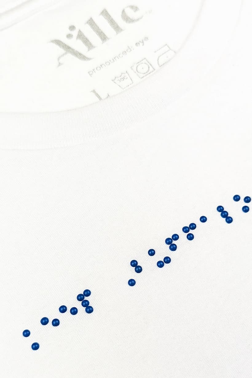 Close up of blue braille beadwork on white t-shirt.