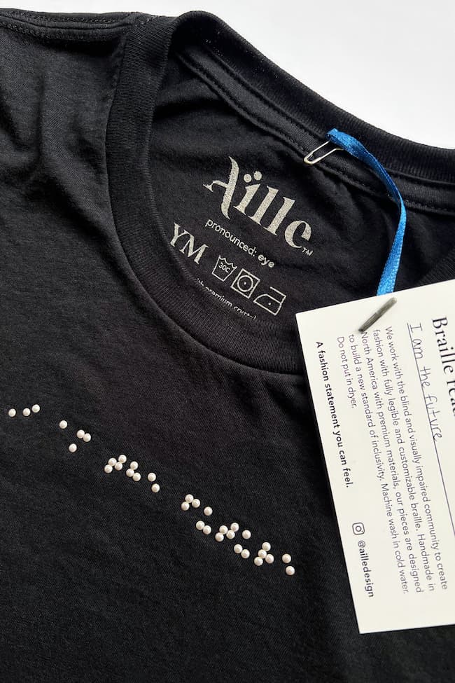 Close up of youth size black braille t-shirt with silver braille that reads "I am the future".